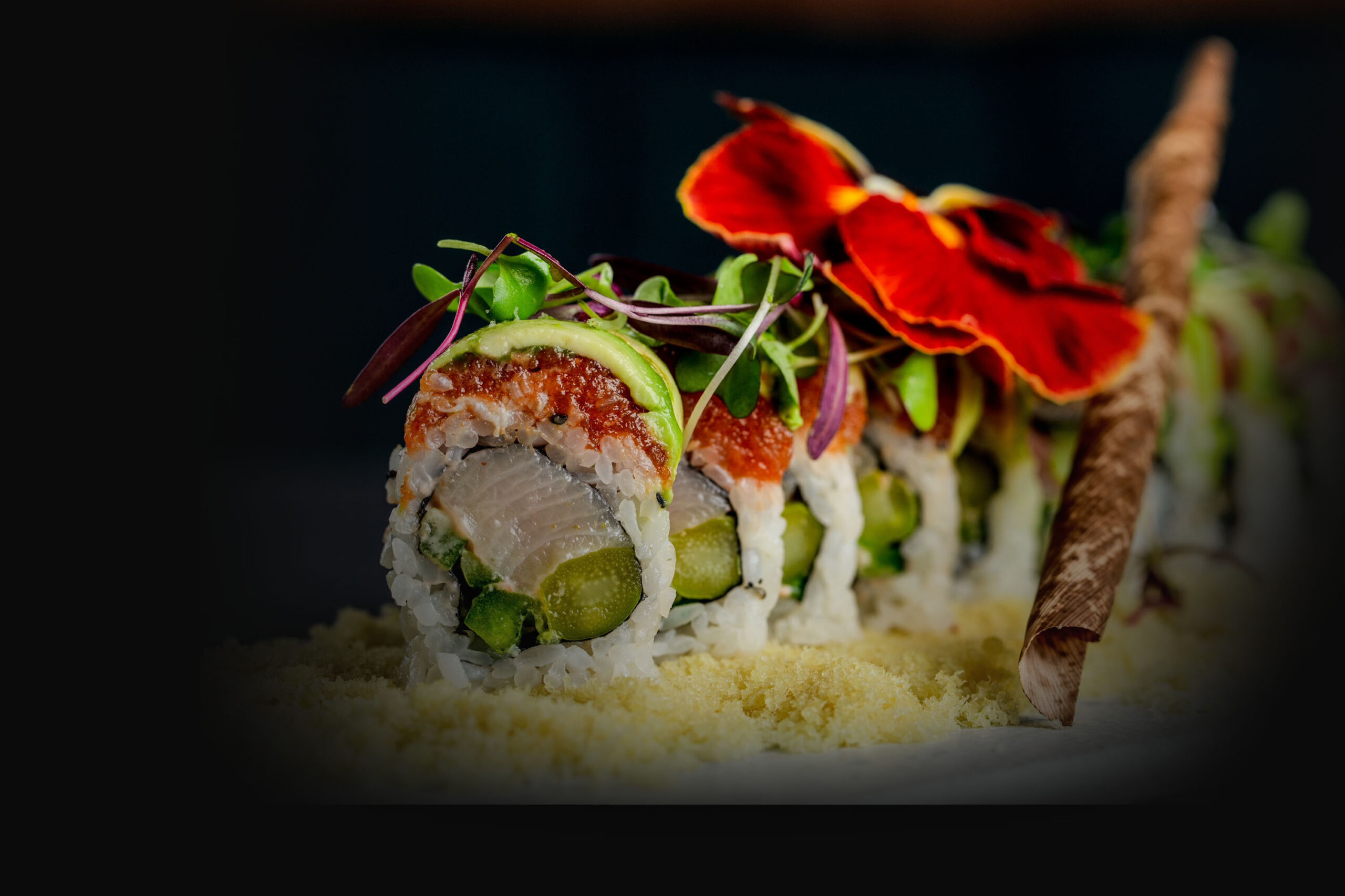 Sushi roll with white fish, asparagus, and spicy tuna, topped with avocado and microgreens