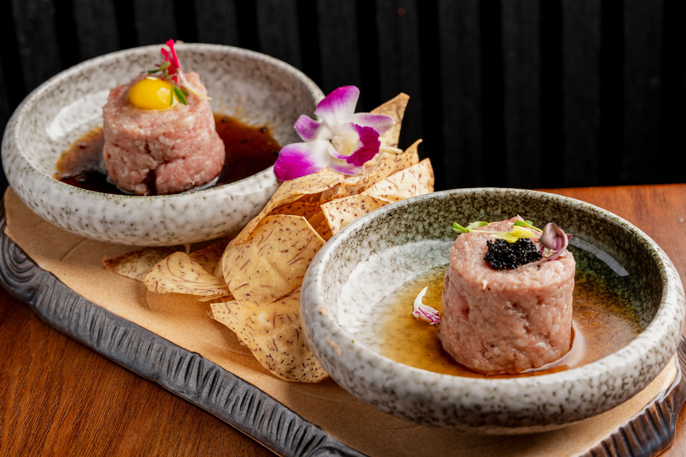 Two bowls of tartare, one topped with a raw quail egg yolk and one with caviar, served with taro chips