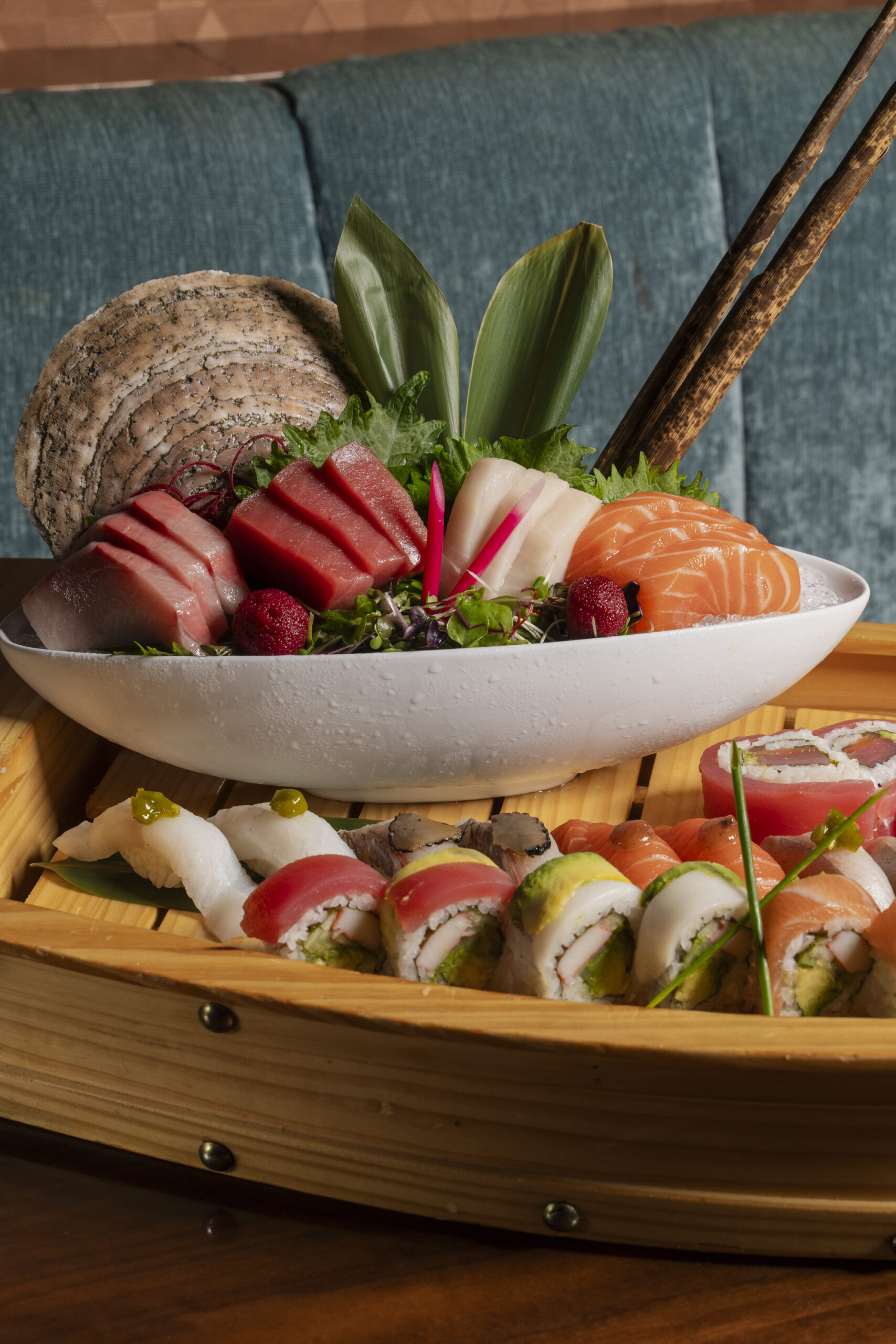 An elaborate sushi boat presentation featuring a bowl of assorted fresh sashimi and a wide variety of sushi rolls and nigiri arranged on the wooden deck