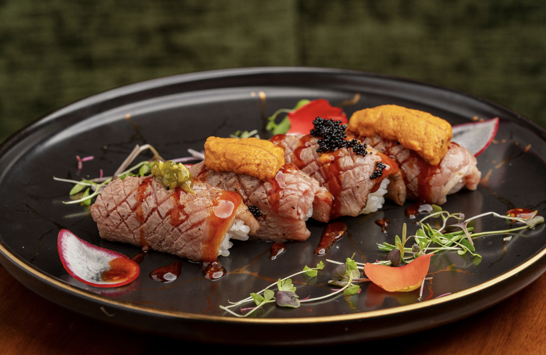 Four seared beef sushi rolls topped with sea urchin and caviar, garnished with microgreens