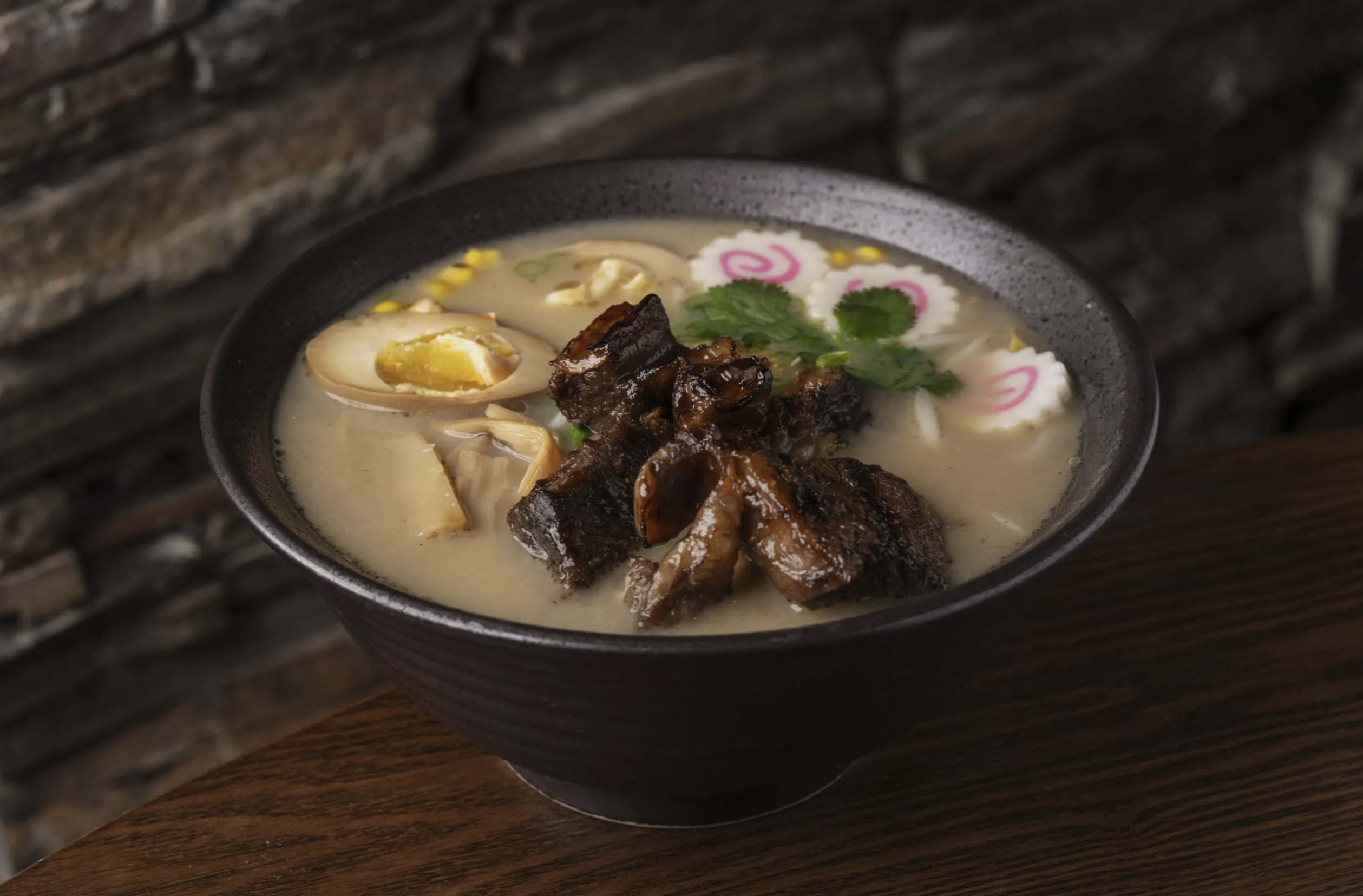 A bowl of creamy ramen topped with dark braised meat and a halved marinated egg